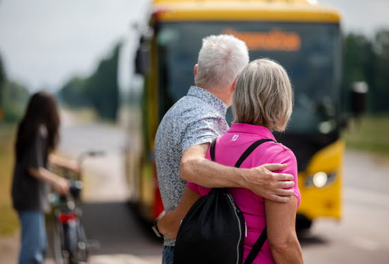 En man håller om en kvinna, samtidigt som bussen anländer till hållplatsen.
