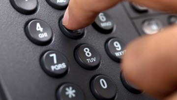 Bordstelefon och ett finger som knappar in telefonnummer.